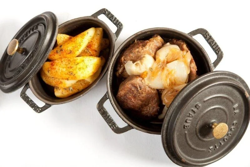 Deux cocottes en fonte : pommes de terre rôties et viande mijotée